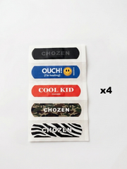 Five bandage-shaped stickers on a white backing sheet, shown on a plain white background. The designs include black, blue with a smiley face, red, camouflage, and black-and-white zebra print.
