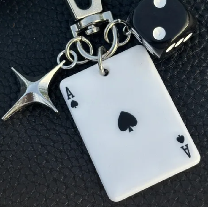 Keychain with ace of spades card, starfish charm, and dice on a dark textured background