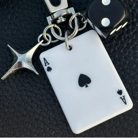 Keychain with ace of spades card, starfish charm, and dice on a dark textured background

